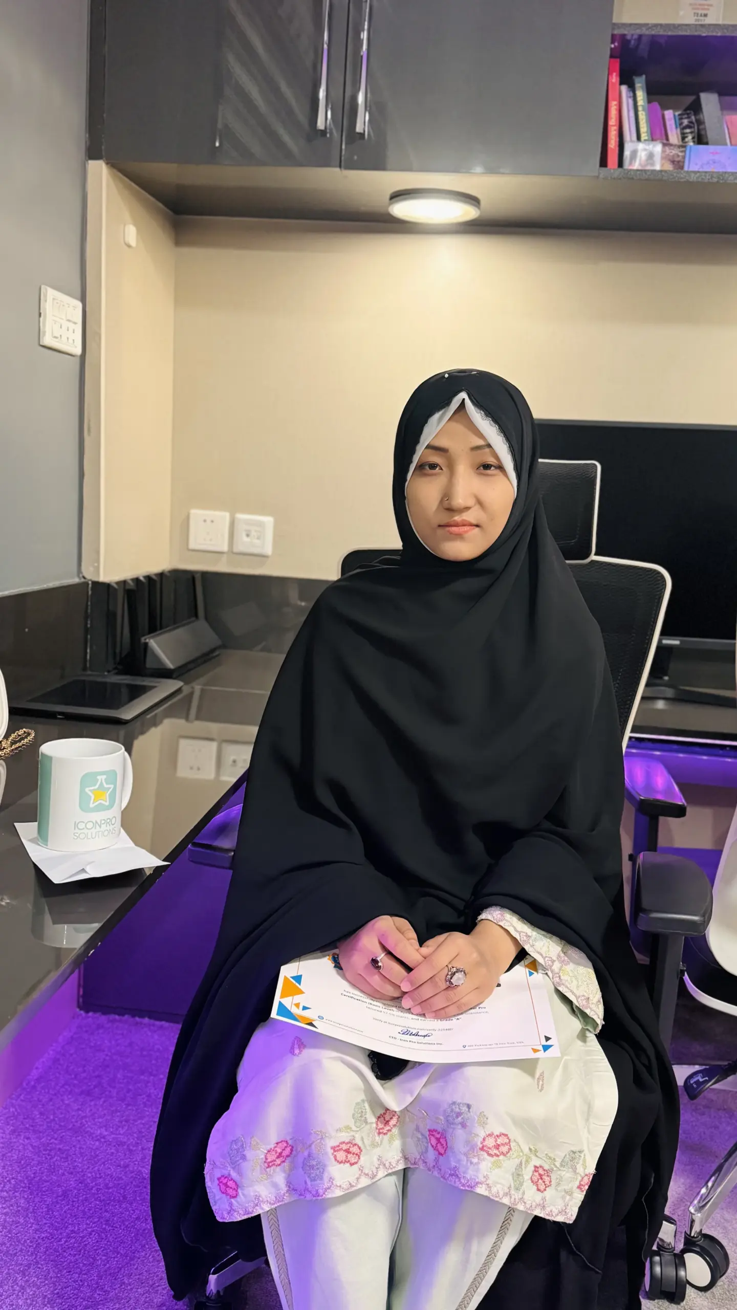A woman in a hijab sits in a modern office, surrounded by corporate