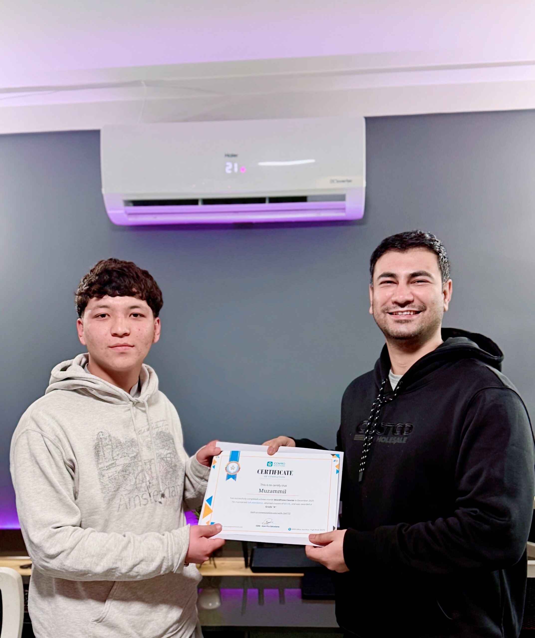 website design Two men holding a certificate in front of a wall with a white air conditioning unit