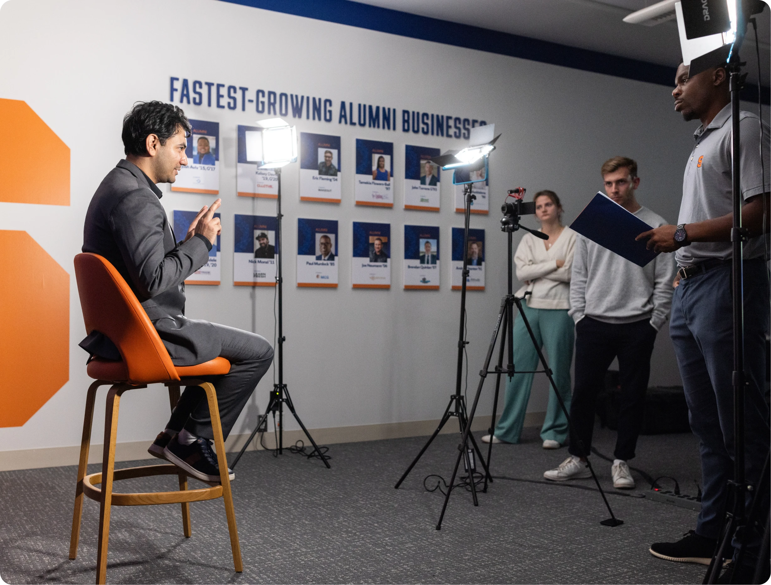 A man sits in a chair in front of a wall with a corporate business website design on it, while others in the background work