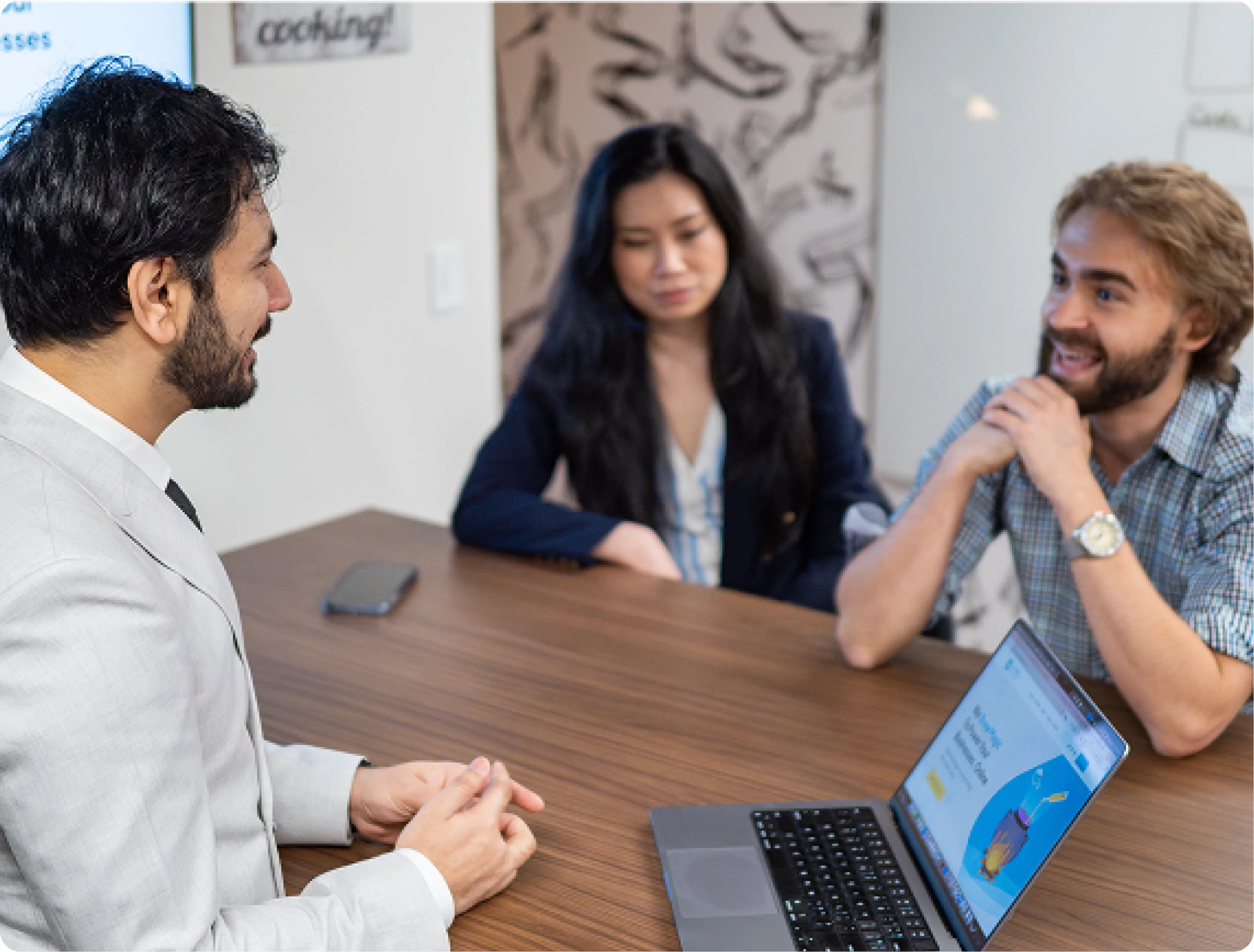 A group of people sitting around a table, looking at a laptop screen with a website design on it, in a corporate setting